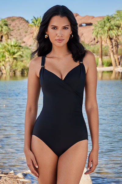 Woman in Miraclesuit Razzle Dazzle Siren Swimsuit in Black standing in a tropical oasis