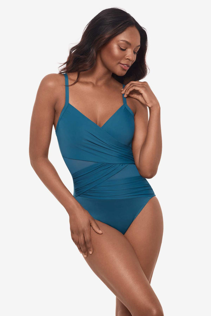 Woman wearing an aegean blue one-piece swimsuit with wrap detailing on the front