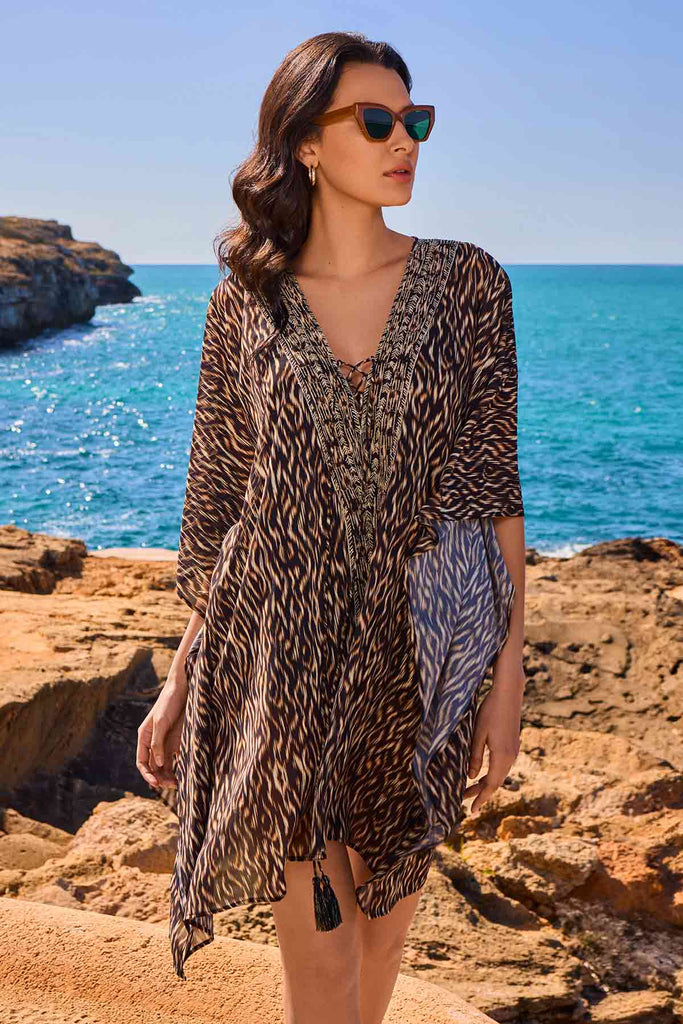 Woman wearing sunglasses facing right wearing multicolored swim cover up in front of beach background